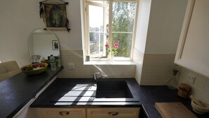 Una cocina con mostrador negro, una ventana con vista a follaje, y un cuenco de fruta sobre el mostrador.