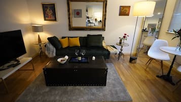 Uma sala de estar moderna com um sofá preto, uma mesa de centro, uma televisão e um espaço de refeições com uma cadeira e mesa.