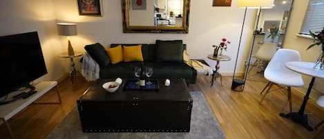 A modern living room with a black sofa, a coffee table, a TV, and a dining area with a chair and table.