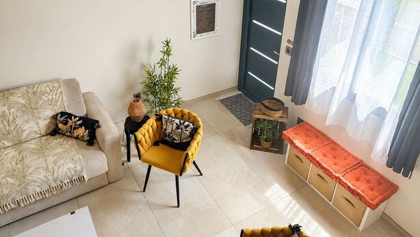A living room with a sofa, a yellow armchair, a small table with a plant, a door, and a window with curtains. - Apartment mountain view, AC - 2 guests (Bras-Panon)