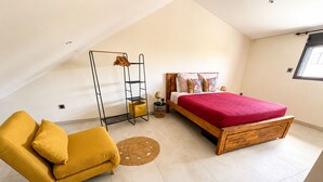 A bedroom with a bed, a yellow armchair, a wooden floor, a ceiling fan, and a window. - Apartment mountain view, AC - 2 guests (Bras-Panon)