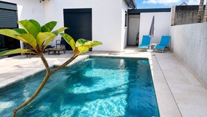 A swimming pool with clear blue water, surrounded by a white building with black shutters, and a few lounge chairs. - Apartment mountain view, AC - 2 guests (Bras-Panon)