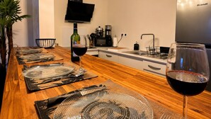 A modern kitchen with a wooden dining table set for six, a wine glass, and a flat-screen TV mounted on the wall. - Apartment mountain view, AC - 2 guests (Bras-Panon)