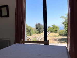 A bed with a view of a chair and greenery outside a window. - House with stunning sea view - 2 guests (Groix)