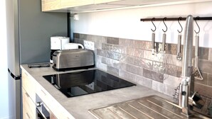 Een keuken met een inbouwtoaster, een koffiezetapparaat en een spoelbak met hangend keukengerei.