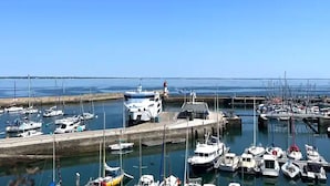 Een jachthaven met diverse boten afgemeerd, een vuurtoren op de achtergrond en een heldere blauwe lucht.