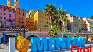 En skylt med ordet ”MENTON” och en stor, gul skulptur föreställande en frukt.