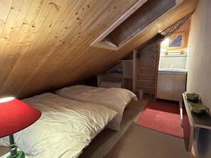 A small attic bedroom with a sloped ceiling, a single bed, a nightstand, a red lamp, and a kitchen area with a sink and cabinets. - Apartment in Méribel, mountain view - 8 guests (Méribel)