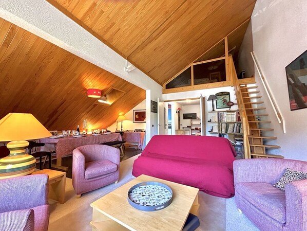 A cozy living room with a high ceiling, wooden beams, a staircase, and a dining area. - Apartment in Méribel, mountain view - 8 guests (Méribel)