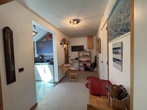A narrow hallway with a kitchen area on the left, a dining area with a red table and chairs, and a living room with a fireplace. - Apartment in Méribel, mountain view - 8 guests (Méribel)