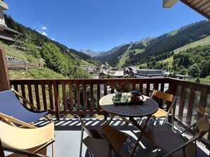 A balcony with a table, chairs, and a view of a valley with houses and mountains. - Apartment in Méribel, mountain view - 8 guests (Méribel)