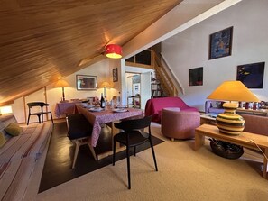 An attic room with a dining table set, chairs, a sofa, and a lamp. - Apartment in Méribel, mountain view - 8 guests (Méribel)