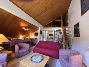 A cozy loft-style living space with a high ceiling, wooden beams, a red sofa, two armchairs, a coffee table, and a bookshelf. - Apartment in Méribel, mountain view - 8 guests (Méribel)