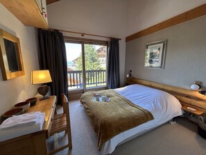 A hotel room with a bed, a desk with a lamp, a chair, a window with curtains, and a picture on the wall. - Apartment in Méribel, mountain view - 8 guests (Méribel)