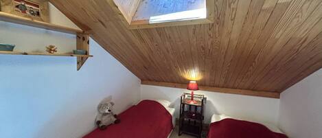A small room with two single beds, a skylight, a table with a lamp, and a teddy bear.