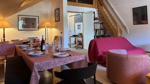 A dining area with a table set for four, a staircase, and a red-covered sofa. - Apartment in Méribel, mountain view - 8 guests (Méribel)