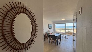Ett rum med ett runt träkonstverk på väggen, en matplats med stolar och ett bord samt en balkong med utsikt över stranden.
