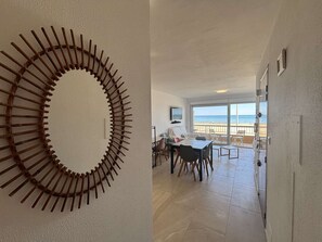 A room with a circular wooden wall art piece, a dining area with chairs and a table, and a balcony with a view of the beach. - Apartment sea view, AC - 4 guests (Port-la-Nouvelle)
