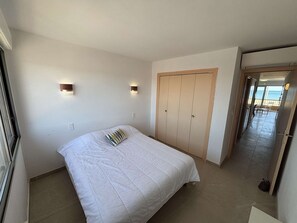 Quarto com cama, guarda-roupa e vista para o mar.