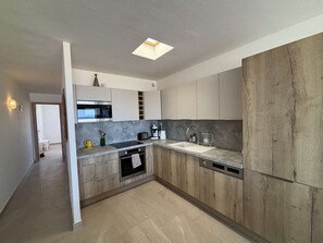 A modern kitchen with a built-in oven, microwave, and sink, featuring light wood cabinetry and a grey countertop. - Apartment sea view, AC - 4 guests (Port-la-Nouvelle)