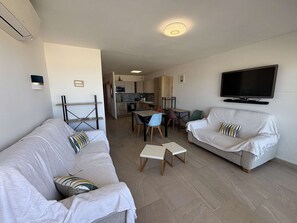 A modern living room with a sofa, a television, and a dining area with chairs and a table. - Apartment sea view, AC - 4 guests (Port-la-Nouvelle)