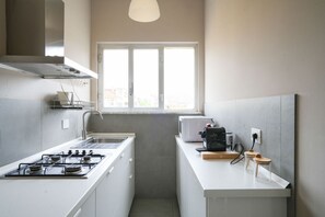 A compact kitchen with a gas stove, microwave, and a window providing natural light. - Torino Centro | Casa Regina (Torino)