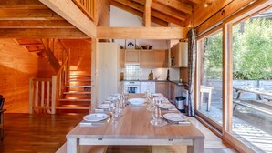 Interior de madera con una mesa de comedor preparada para seis personas, una zona de cocina y ventanas amplias.
