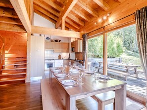 A wooden cabin with a dining area set for a meal, a kitchen, and large windows overlooking a forested area. - Cozy chalet near slopes - 8 guests (Le Grand-Bornand)