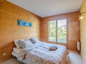 Ein Zimmer mit Holzwänden, einem Bett, einem Fenster und einem Gemälde an der Wand.