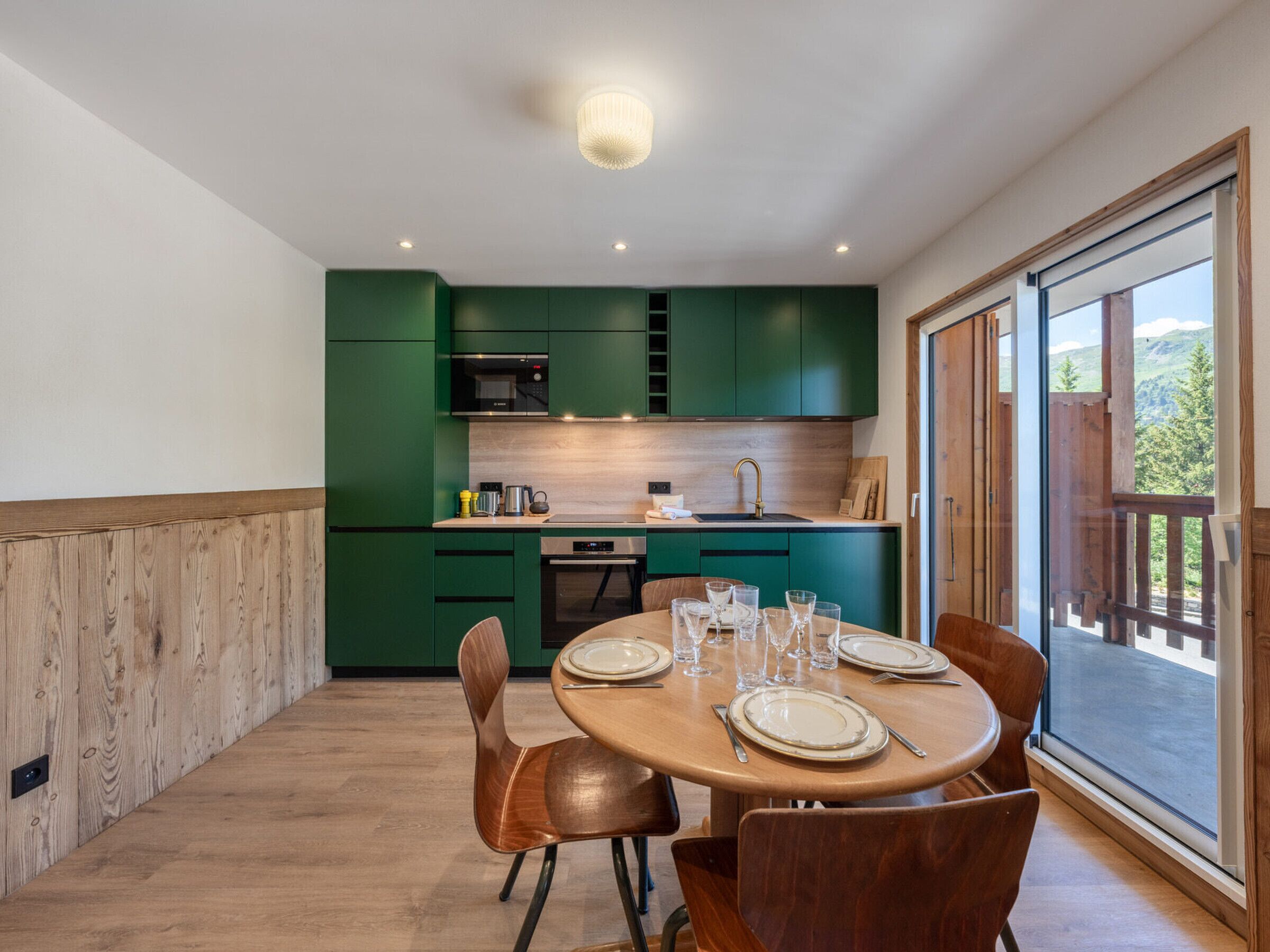 Una cocina moderna con armarios verdes, una mesa de comedor para cuatro personas y un amplio ventanal con vistas al exterior.