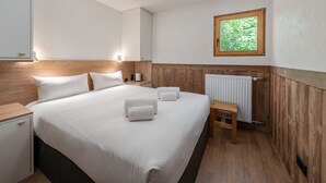 Une chambre d’hôtel avec un lit, des tables de chevet, une fenêtre donnant sur un espace verdoyant et un radiateur.