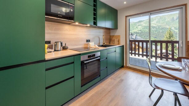 Une cuisine moderne avec des meubles verts, un four à micro-ondes Bosch et une vue sur un paysage montagneux grâce à une grande porte-fenêtre coulissante.