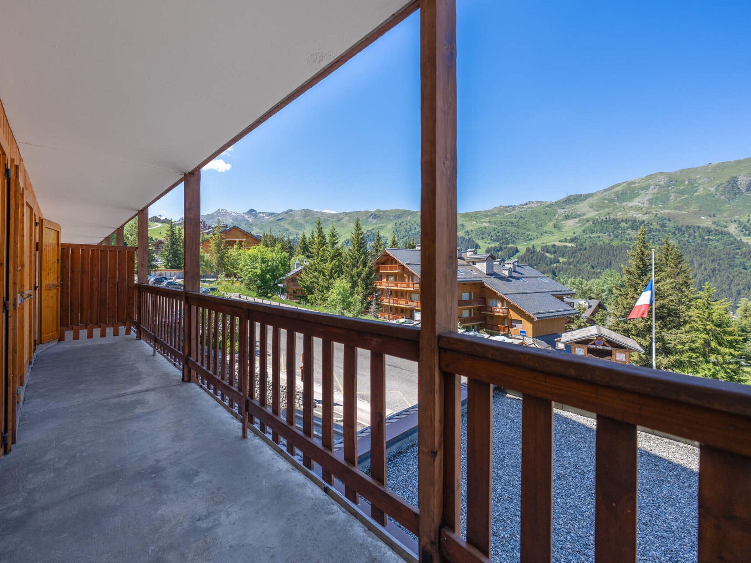 A wooden balcony with a view of mountain houses and a flag.
