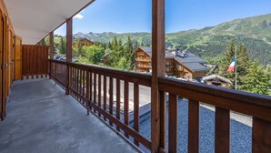Un balcon en bois offrant une vue sur des maisons de montagne et sur un drapeau.