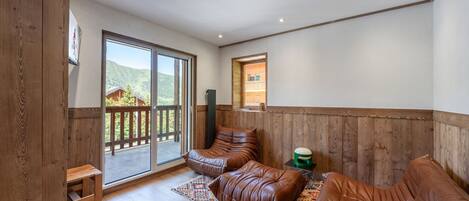 Una habitación amplia con un gran ventanal corredero que da a un balcón, un sofá de cuero marrón, una pequeña mesa de madera y una alfombra estampada.