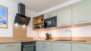 Eine moderne Küche mit integriertem Backofen, Mikrowelle und Kaffeemaschine, Holzschränken und einer Edelstahl-Dunstabzugshaube.