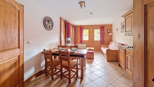 A wooden interior with a dining table, chairs, a sofa, and a kitchen area. - Spacious apartment with balcony and parking, close to slopes (Les Menuires)