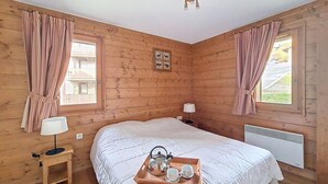 A wooden room with a bed, a bedside table with a lamp, and a tray with cups and a kettle. - Spacious apartment with balcony and parking, close to slopes (Les Menuires)