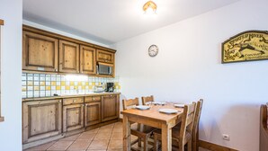 Una cucina con mobili in legno, un forno a microonde, piastrelle a parete, un tavolo da pranzo con sedie e una sveglia a parete.