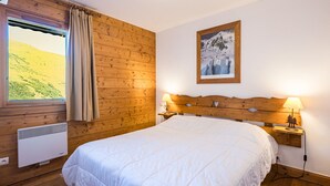 Una camera da letto con una testiera in legno, un letto con biancheria da letto bianca, una finestra con tende, un condizionatore d'aria a parete e un quadro incorniciato appeso al muro.