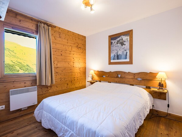 Een slaapkamer met een houten hoofdbord, een bed met wit bedlinnen, een raam met gordijnen, een wandairconditioner en een ingelijst schilderij aan de muur.