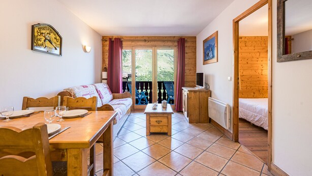 Um quarto aconchegante com piso de madeira, um sofá, uma mesa de jantar com cadeiras, um pequeno armário e uma cama.