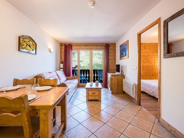 A cozy room with a wooden floor, a sofa, a dining table with chairs, a small cabinet, and a bed. - Bright apartment near the slopes - 4 guests (Les Menuires)