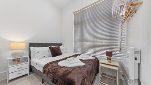 Um quarto moderno com uma cama, mesas de cabeceira, uma luminária e uma janela com persianas.