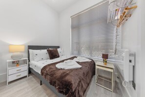 Ein modernes Schlafzimmer mit einem Bett, Nachttischen, einer Lampe und einem Fenster mit Jalousien.