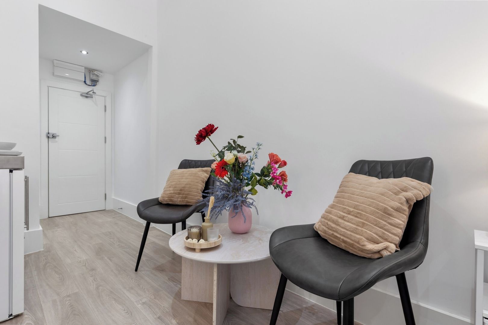 A modern room with two black leather chairs, a small round table with a vase of flowers, and a white door.