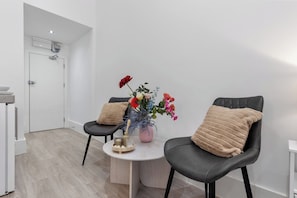 A modern room with two black leather chairs, a small round table with a vase of flowers, and a white door.