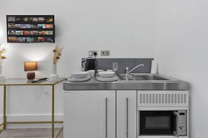 A modern kitchen with a built-in microwave, a stainless steel sink, and a flat-screen TV mounted on the wall displaying various shows.