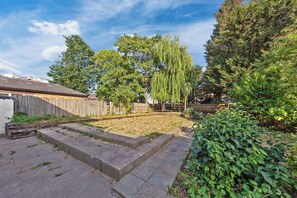 A backyard with a concrete play area, a wooden fence, and various trees.