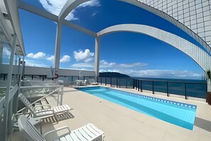 A pool area with lounge chairs and a clear view of the ocean. - SHB Magia de uma Vista Panorâmica (Santos)